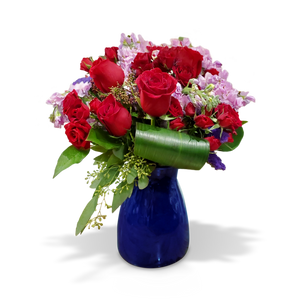 Elegant floral arrangement featuring vibrant red roses and soft lilac blooms, accented with lush greenery in a striking blue vase. A perfect gift for romantic occasions, anniversaries, or special celebrations, available at Chez Joy Florist.