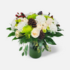 Winter floral arrangement featuring white hydrangeas, cream roses, green chrysanthemums, pinecones, and festive accents in a green vase. Perfect for holiday décor or gifting, available at Chez Joy Florist.